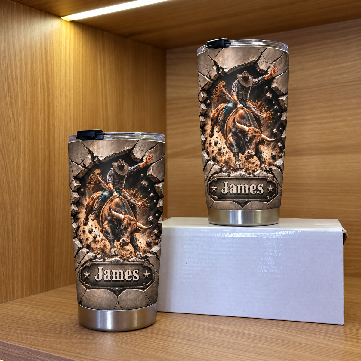 Two personalized western rodeo tumblers featuring a bull rider graphic, displayed on a wooden shelf in different sizes.