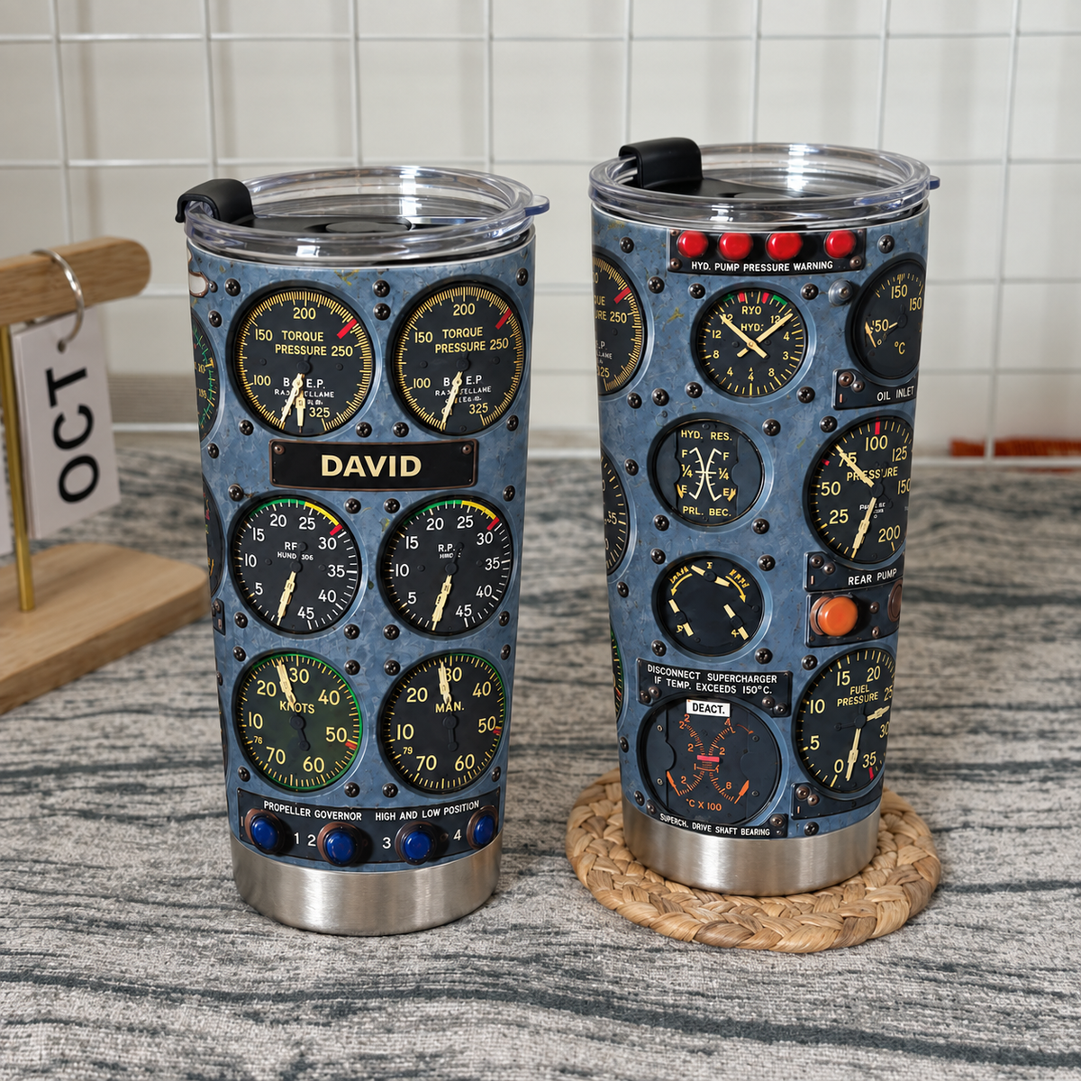 Two cockpit instrument panel tumblers standing on a textured surface in front of a white wire grid.