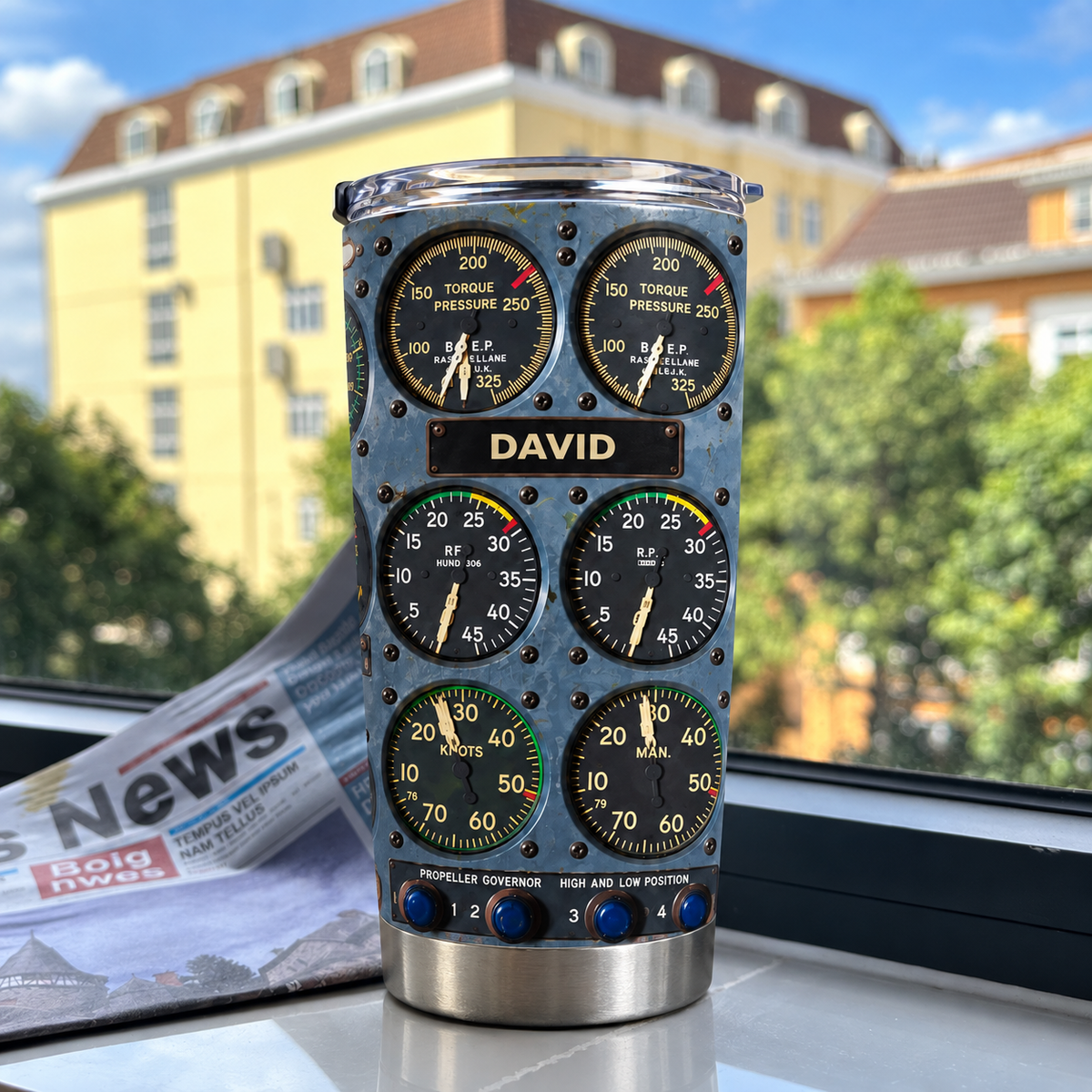Cockpit instrument panel tumbler with custom name David standing upright on a windowsill overlooking buildings.