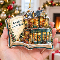 Hand holding a clear acrylic book ornament with a custom bookstore scene and holiday lights.