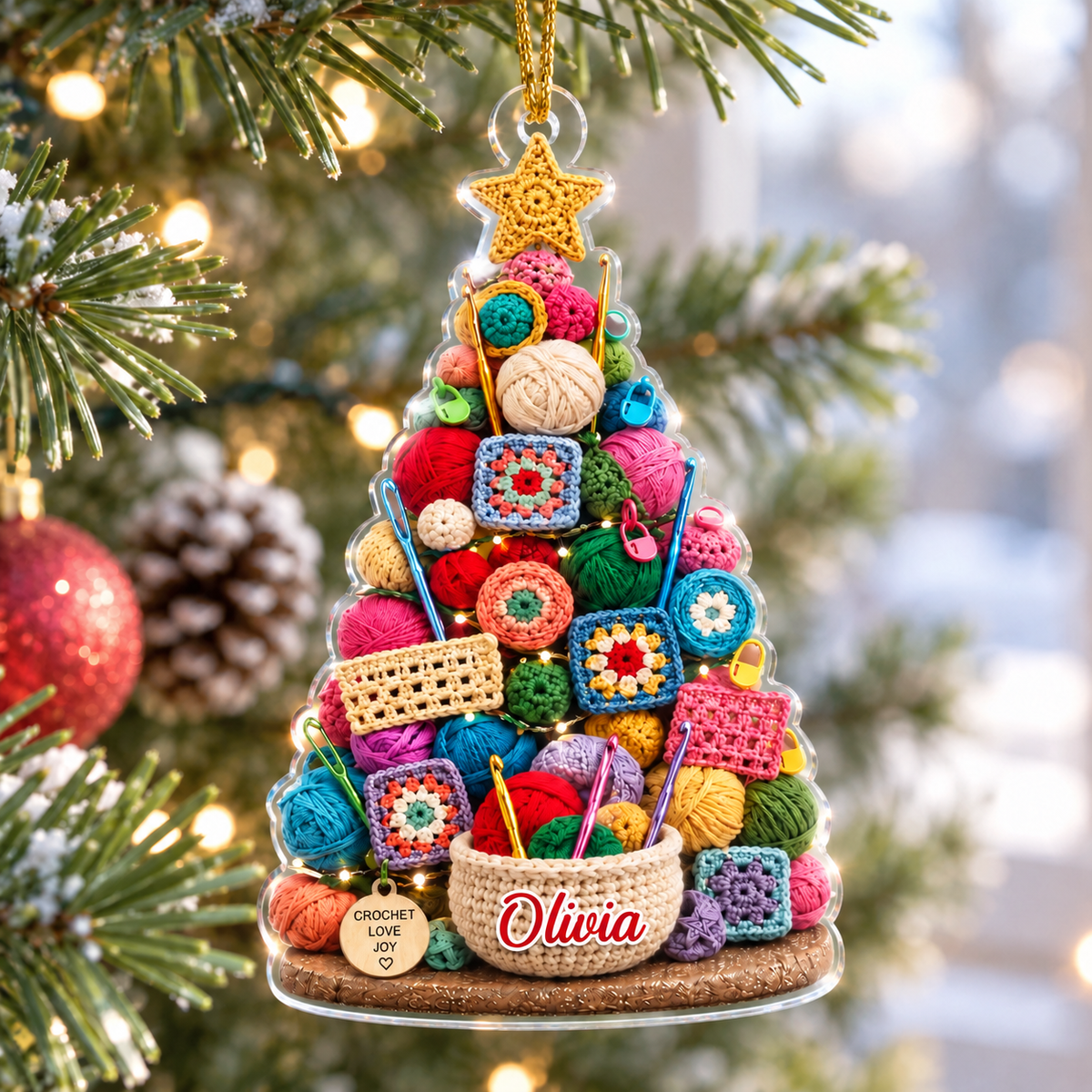 Personalized acrylic Christmas tree ornament featuring colorful yarn balls, granny squares, and a custom name tag on a pine