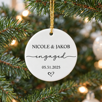 Custom map engagement ornament hanging on a lit Christmas tree branch with warm glowing lights in the background.