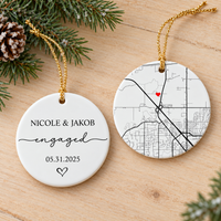 Two-sided ceramic engagement ornament showing front text and back map with red heart on wooden table with pine branches.