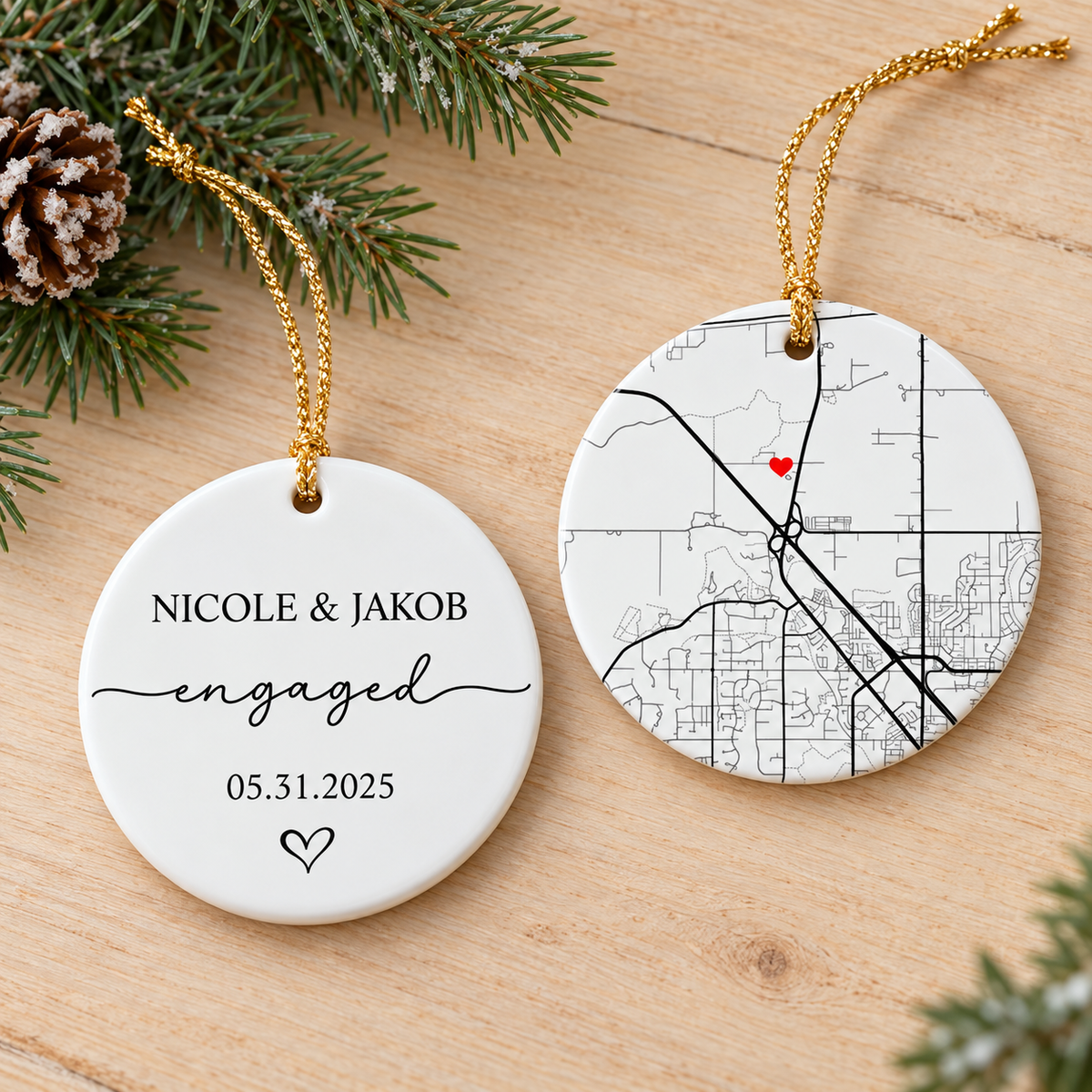 Two-sided ceramic engagement ornament showing front text and back map with red heart on wooden table with pine branches.