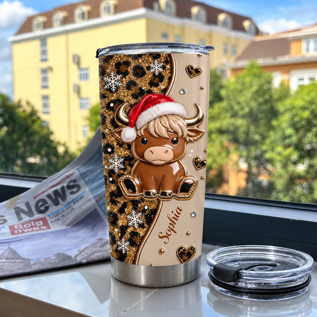 Personalized Christmas highland cow leopard print tumbler with name Sophia and lid on table against blurred building
