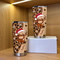 Two personalized Christmas highland cow leopard print tumblers with name Sophia on white box on wooden shelf.