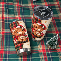 A personalized Christmas Highland cow tumbler with a black lid resting beside a small artificial pine tree on a green plaid