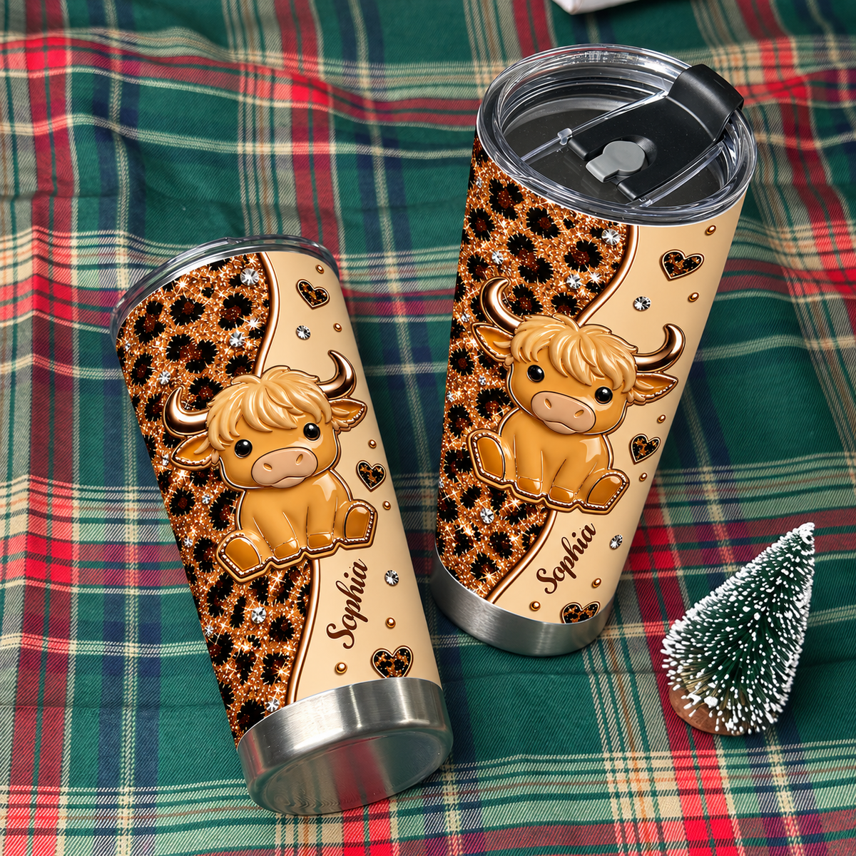 Two personalized stainless steel cups with western aesthetic on a green plaid blanket next to a tree.