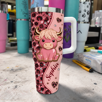 A 40oz custom name tumbler with a pink leopard print design and a cute baby highland cow standing in a workshop.