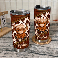 Two cute Highland cow tumblers with custom names displayed on a textured surface next to a small wooden calendar