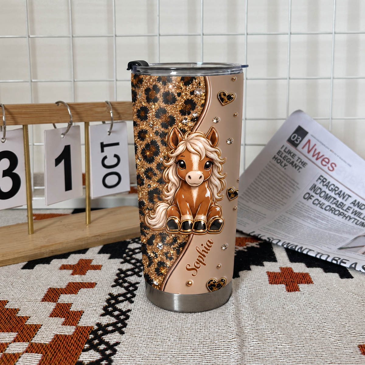Personalized horse tumbler with cute pony and leopard print standing on woven mat beside calendar block and newspaper.