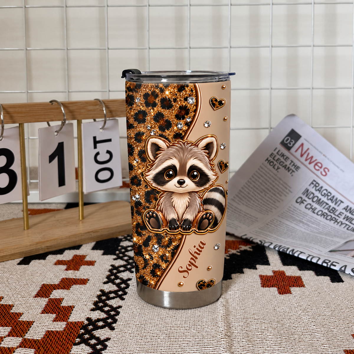A cute raccoon leopard print cup with custom text stands on a patterned mat next to a wooden calendar showing October.