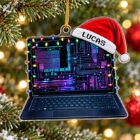 Personalized laptop ornament hanging on a festive Christmas tree with glowing lights and pine needles.