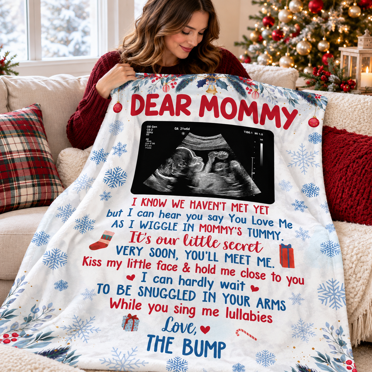Expecting mother sitting on a couch and holding up a custom Dear Mommy blanket with ultrasound photo.