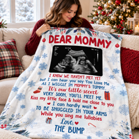 Expecting mother sitting on a couch and holding up a custom Dear Mommy blanket with ultrasound photo.