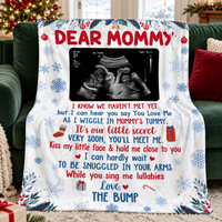 Pregnancy announcement blanket with snowflake design and ultrasound photo laid across a green sofa.