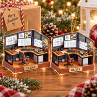 Two custom name ornaments with wood finish base and printed corner desk scene displayed next to a wrapped Christmas gift.