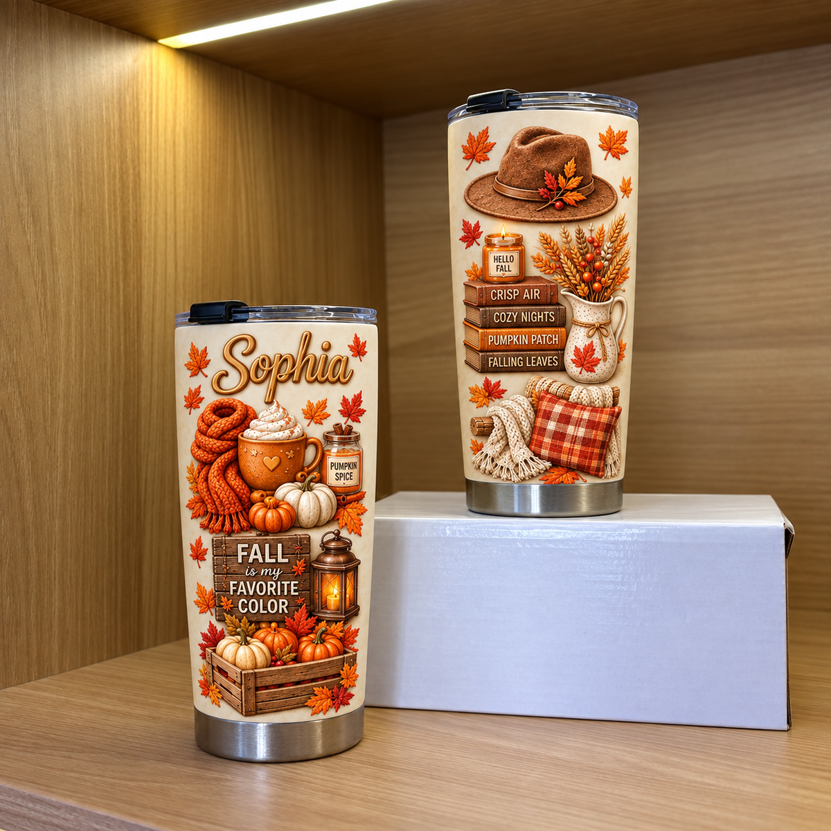 Two custom stainless steel tumblers with fall themes displayed on shelves inside a wooden cabinet.