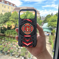 A hand holding a personalized firefighter tough phone case outdoors with green trees and buildings in the blurred background.