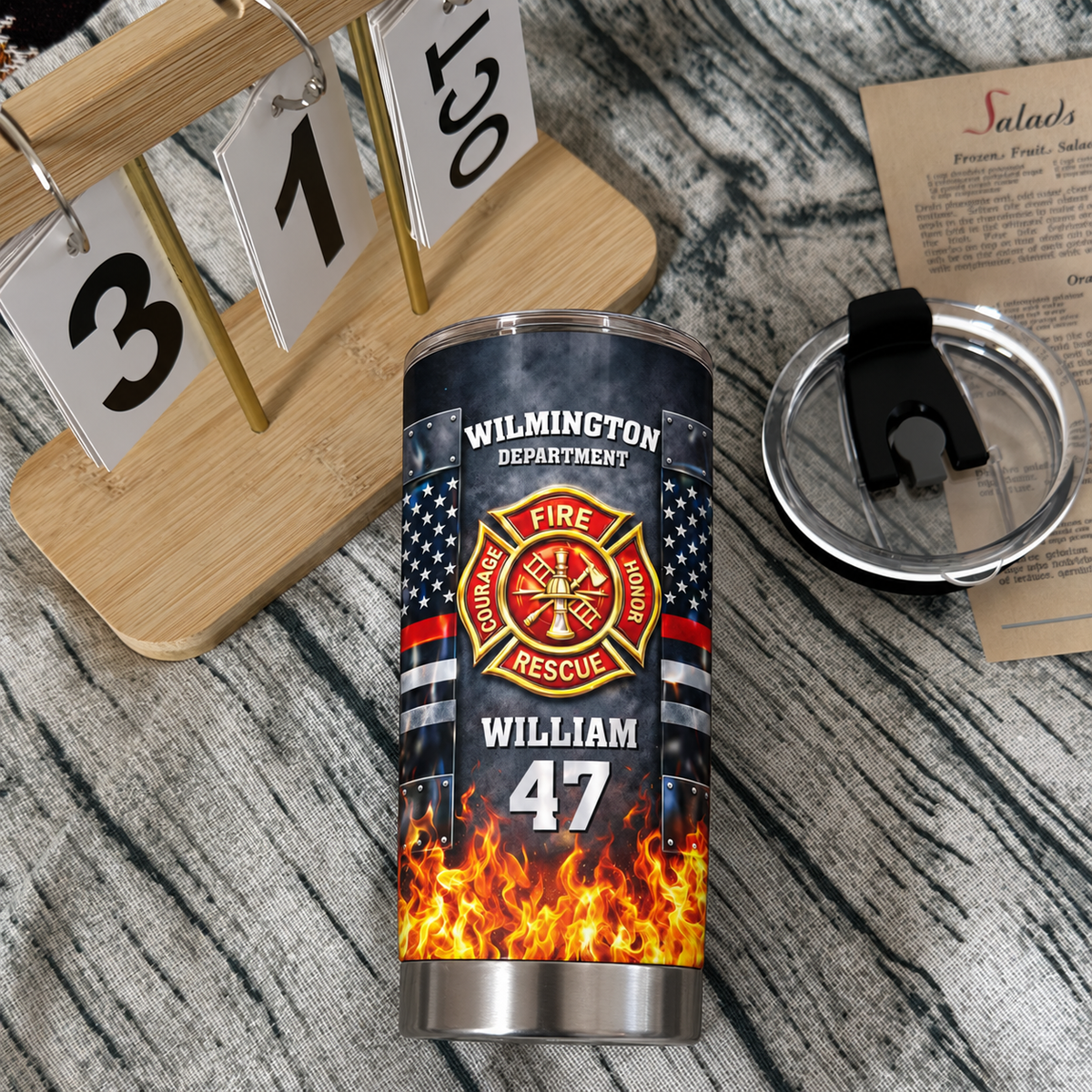 Personalized firefighter stainless steel tumbler next to a wooden block calendar showing October 31 and a menu card.
