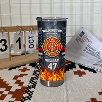 Personalized firefighter travel tumbler standing upright on a textured woven mat with a wooden calendar and open newspaper.