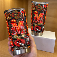 A hand holds up a personalized firefighter initial name tumbler against a wooden surface and gift box.