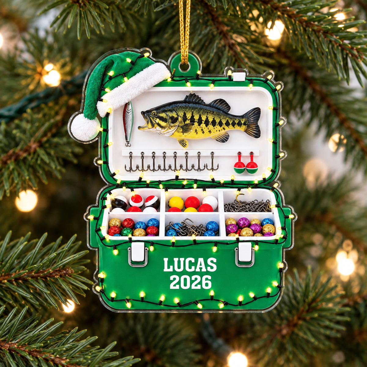 Fishing tackle box ornament in green, featuring bass fish, Santa hat, and custom name LUCAS 2026 hanging on a Christmas tree.