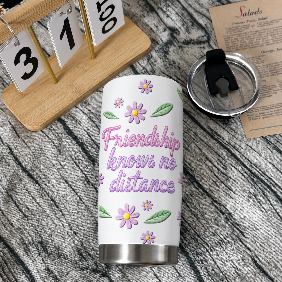 A custom name travel mug standing on a wooden tabletop next to a wooden desk calendar and a black plastic lid.