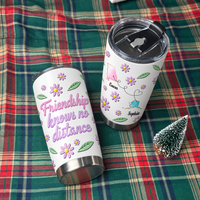 Two long distance friendship gift tumblers placed on a green plaid fabric with a small miniature Christmas tree.