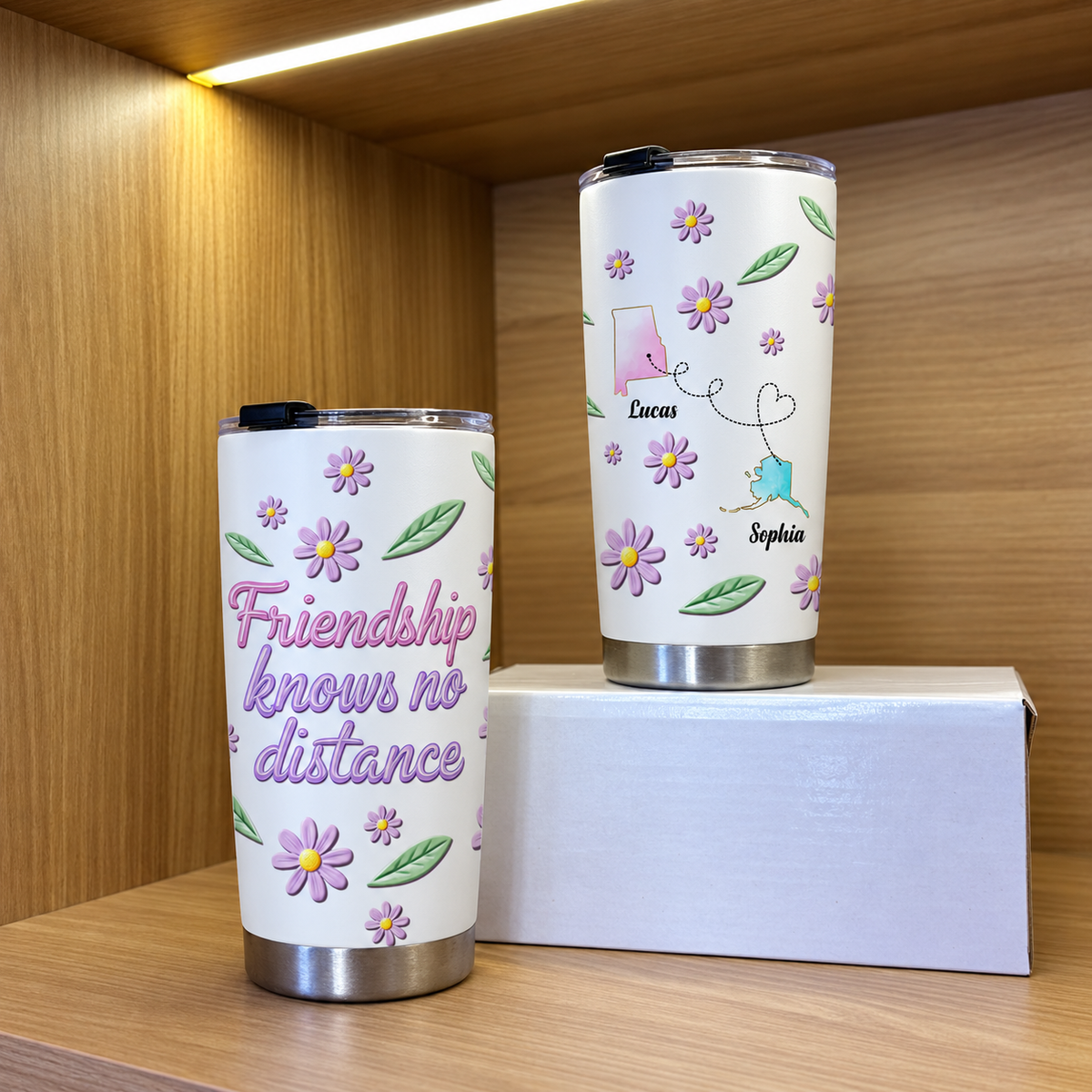 Two white floral stainless steel cups on a wooden shelf, one showing quote and the other showing custom state map travel mug