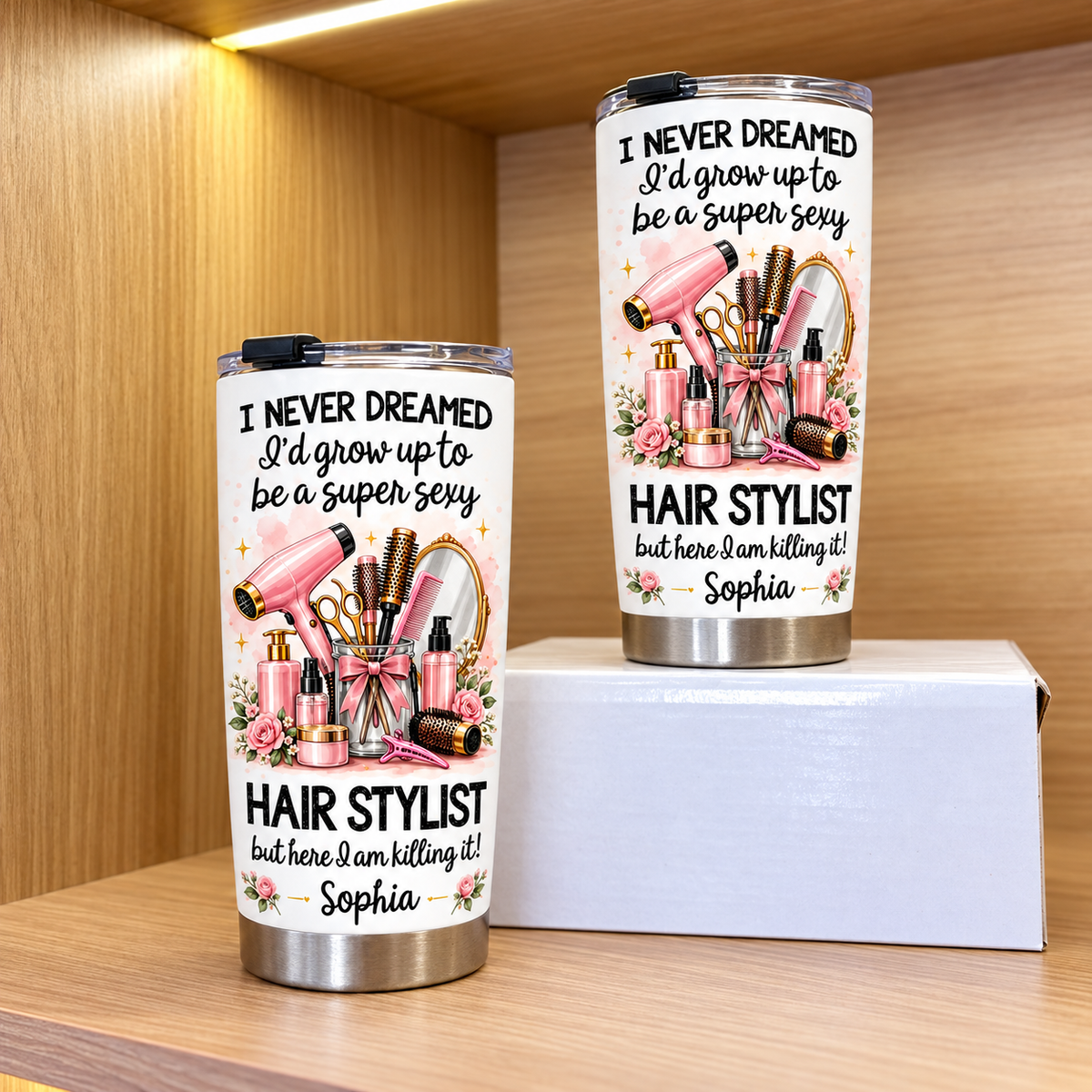 Two personalized funny hairstylist tumblers displayed on wooden shelves with white boxes.