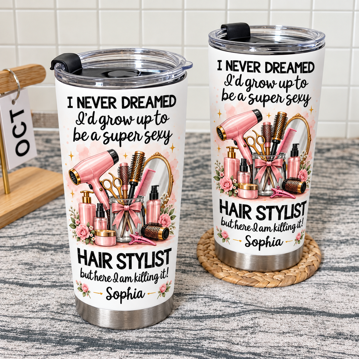 Two personalized funny hairstylist tumblers standing on a textured surface with a tiled wall backdrop.