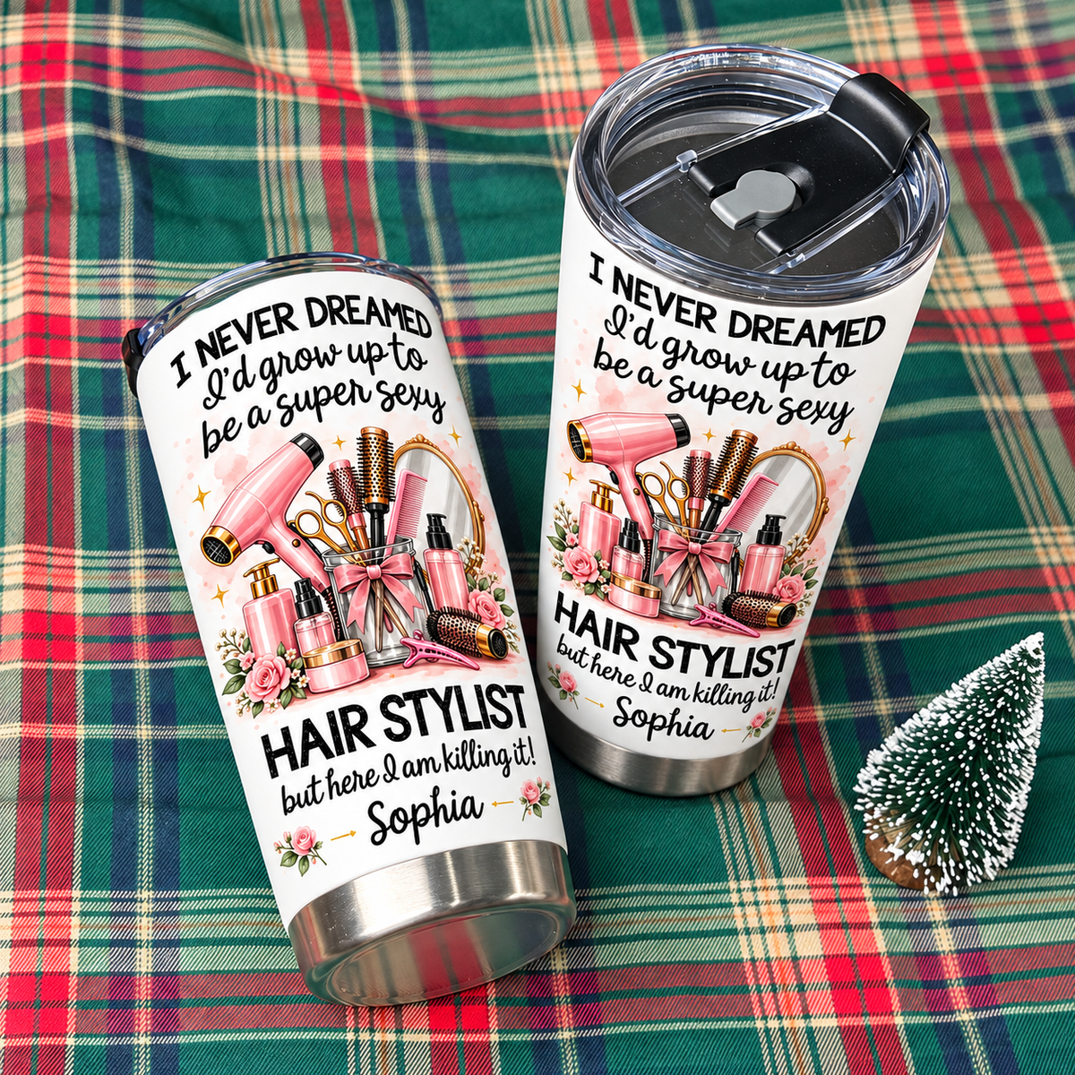 Two personalized funny hairstylist tumblers displayed on a green plaid fabric with a small decorative tree.