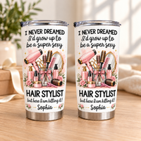Two personalized funny hairstylist tumblers standing on a wooden tabletop in front of a soft-focus background.