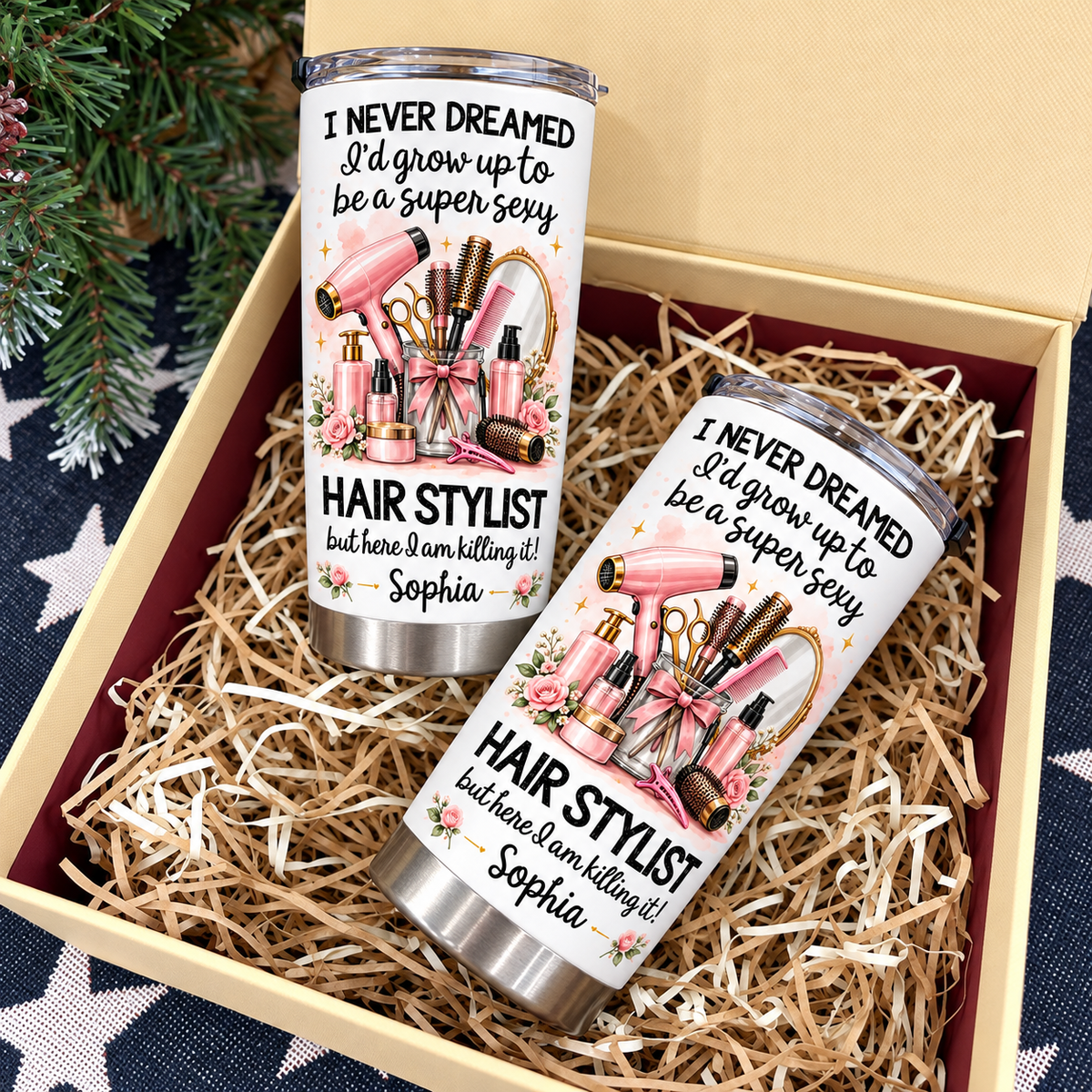 Two personalized funny hairstylist tumblers presented inside an open gift box filled with shredded paper.