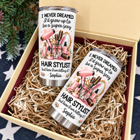 Two personalized funny hairstylist tumblers presented inside an open gift box filled with shredded paper.