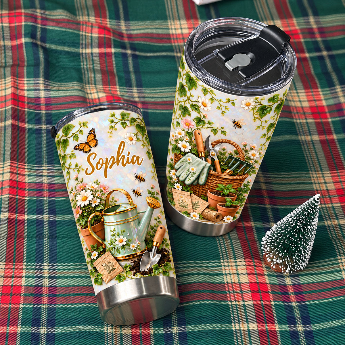 Two gardening theme personalized tumblers displayed on a green plaid fabric cloth next to a miniature evergreen tree.