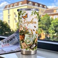 Botanical tumbler featuring custom name Sophia and garden tools displayed on a windowsill with a newspaper and buildings