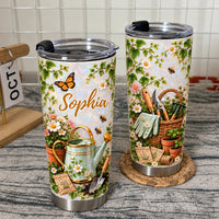 Two personalized garden tumblers with watering can and flower basket illustrations on a counter with calendar block backdrop.