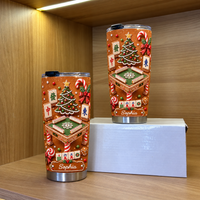 Two custom name stainless steel tumblers with gingerbread mahjong design on a white box inside a wooden cabinet.