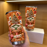 Two personalized Gingerbread Mahjong Christmas Tumblers displayed on a wooden shelf next to a white box.