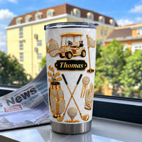 Custom name tumbler with a gold golf theme displayed on a windowsill with a newspaper.