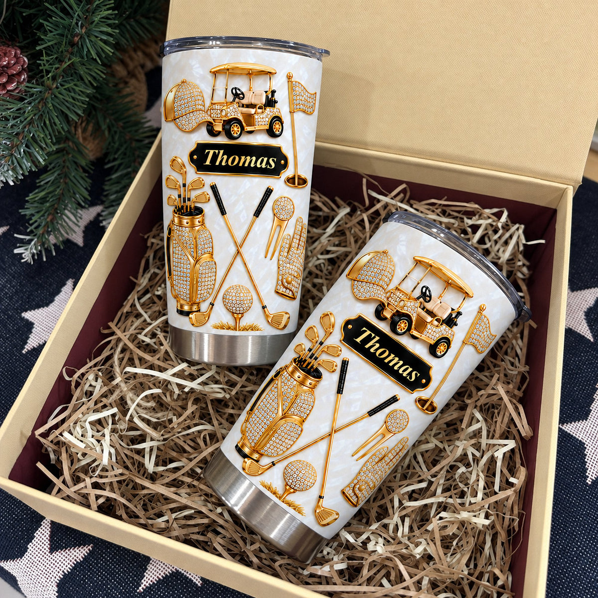Two personalized golf tumblers arranged in a gift box lined with paper shreds.