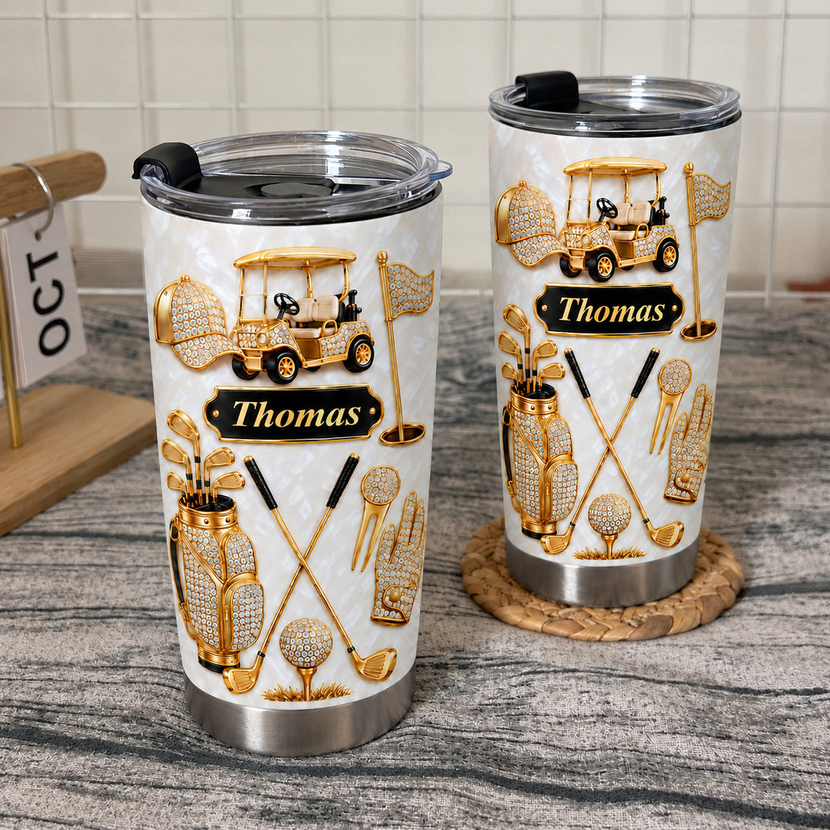 Two stainless steel tumblers with a gold golf cart design standing on a light wooden table.