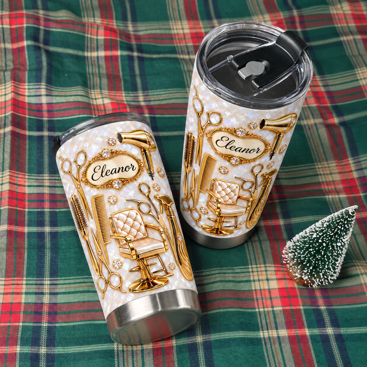 A custom name hair stylist gift stainless steel travel mug rests on a red plaid blanket next to a small tree.