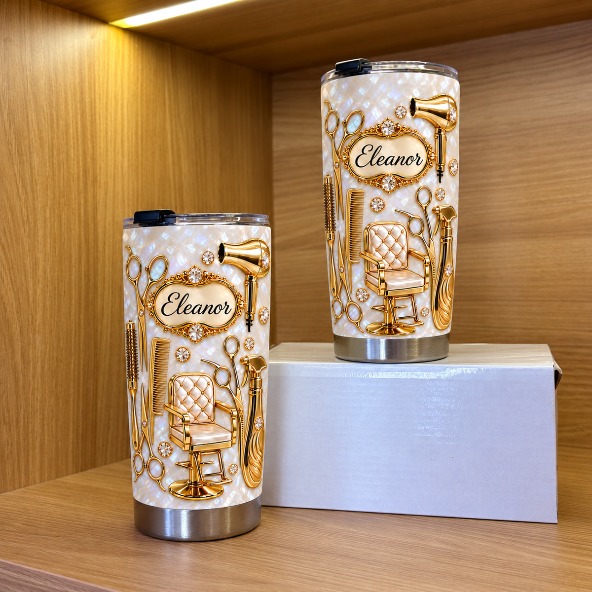 Two personalized stainless steel travel mugs with gold salon chair motifs stand inside a wooden shelving unit.