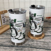 Two custom name tumblers featuring golf equipment flat lay design standing on a rustic wood surface