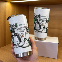 Hand holding Golf Equipment Flat Lay Tumbler against a warm wood background with a box behind it
