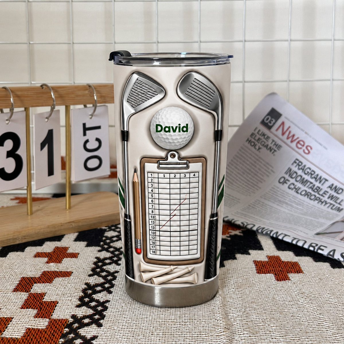 Stainless steel insulated golf mug featuring a scorecard clipboard design, set indoors near a calendar.