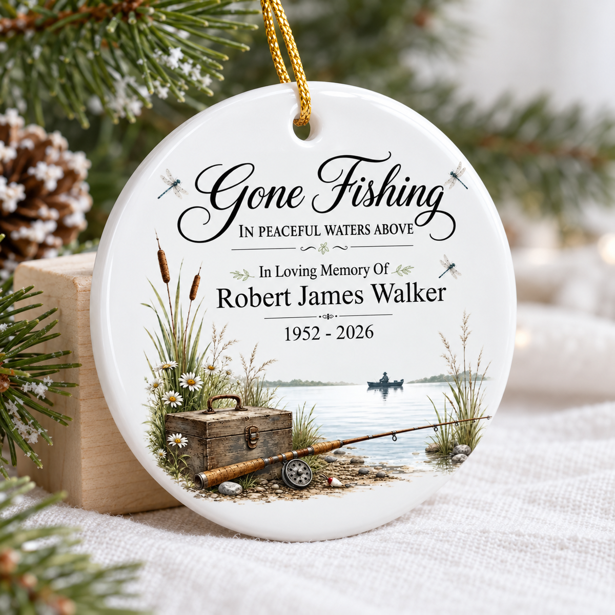Personalized memorial ornament leaning against a small wooden block surrounded by pine and warm lights